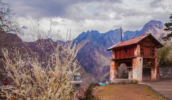 उत्तराखंड मौसम पूर्वानुमान के बीच पहाड़ी सड़क के किनारे एक झोपड़ी और आसमान में उमड़ते काले बादल